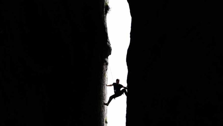 Choose your suffering: A man climbing up between two rocks.